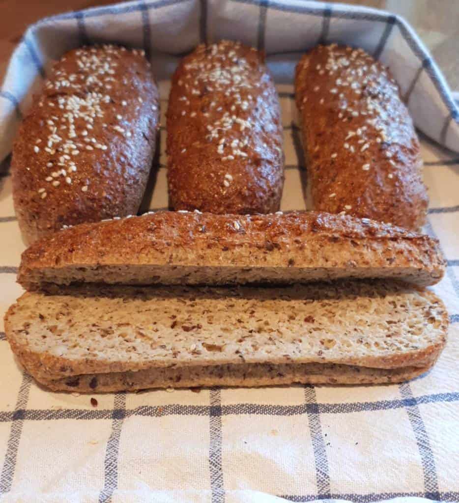 Fyra fullkornsbröd med sesamfrön på en rutad kökshandduk, ett bröd är skuret på mitten.
